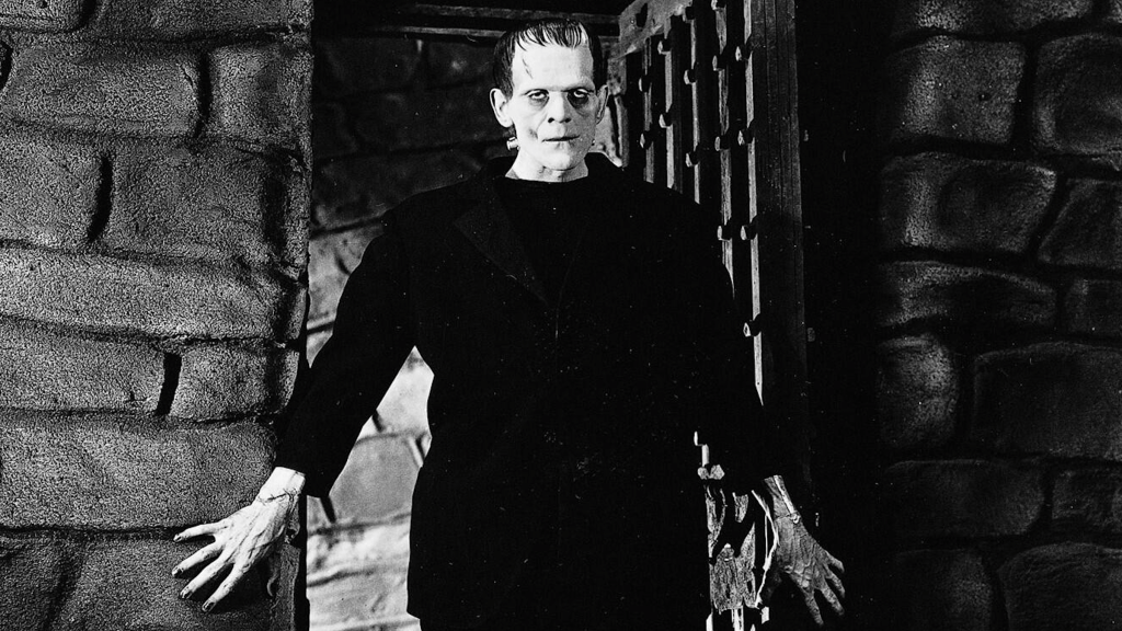 Black and white still from the film Frankenstein featuring Frankenstein's monster walking through a door.