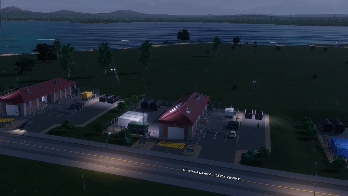 A streetview image of a groundwater pumping station at night. A ways behind it, a body of water is visible.