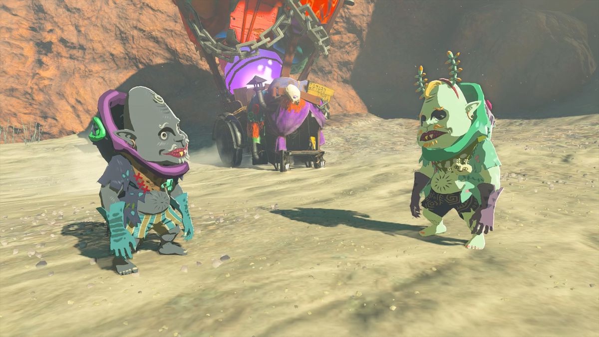 Koltin, a small green humanoid creature with horns, stands with his brother, a grey humanoid creature, in a desert landscape. 